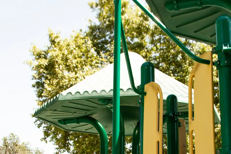 Sunlit playground equipment with green slides and shaded platforms